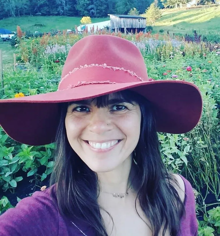 Briana J. Sabaj, LAc. MSTOM, smiling in a wide-brimmed rose hat with a flower field behind her