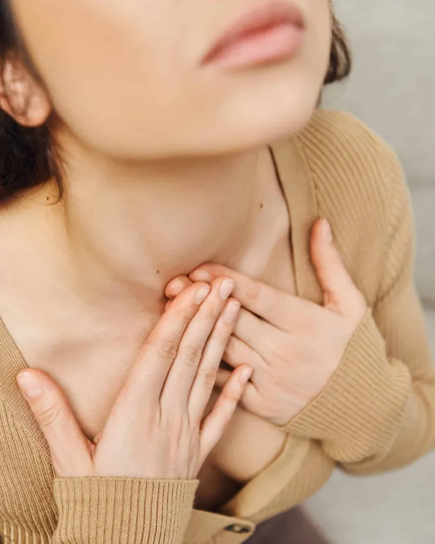 Woman resting her fingertips at the base of her throat, over the thyroid and lymph points