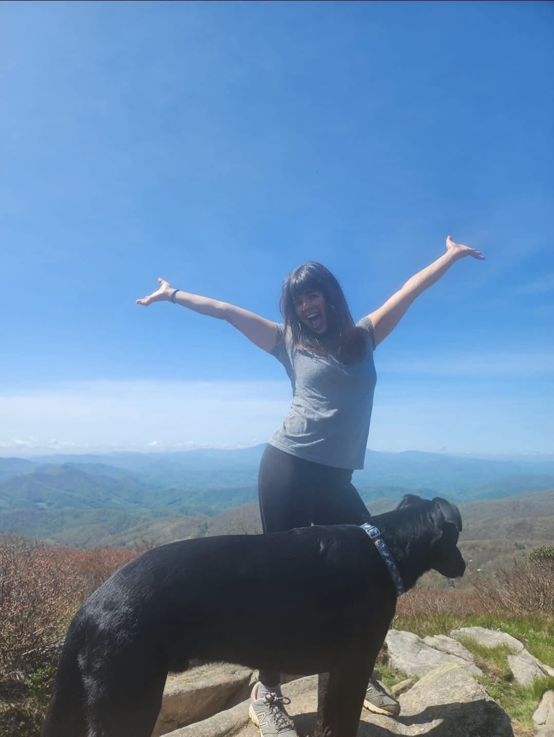 Briana on a Blue Ridge summit, arms raised, with her dog