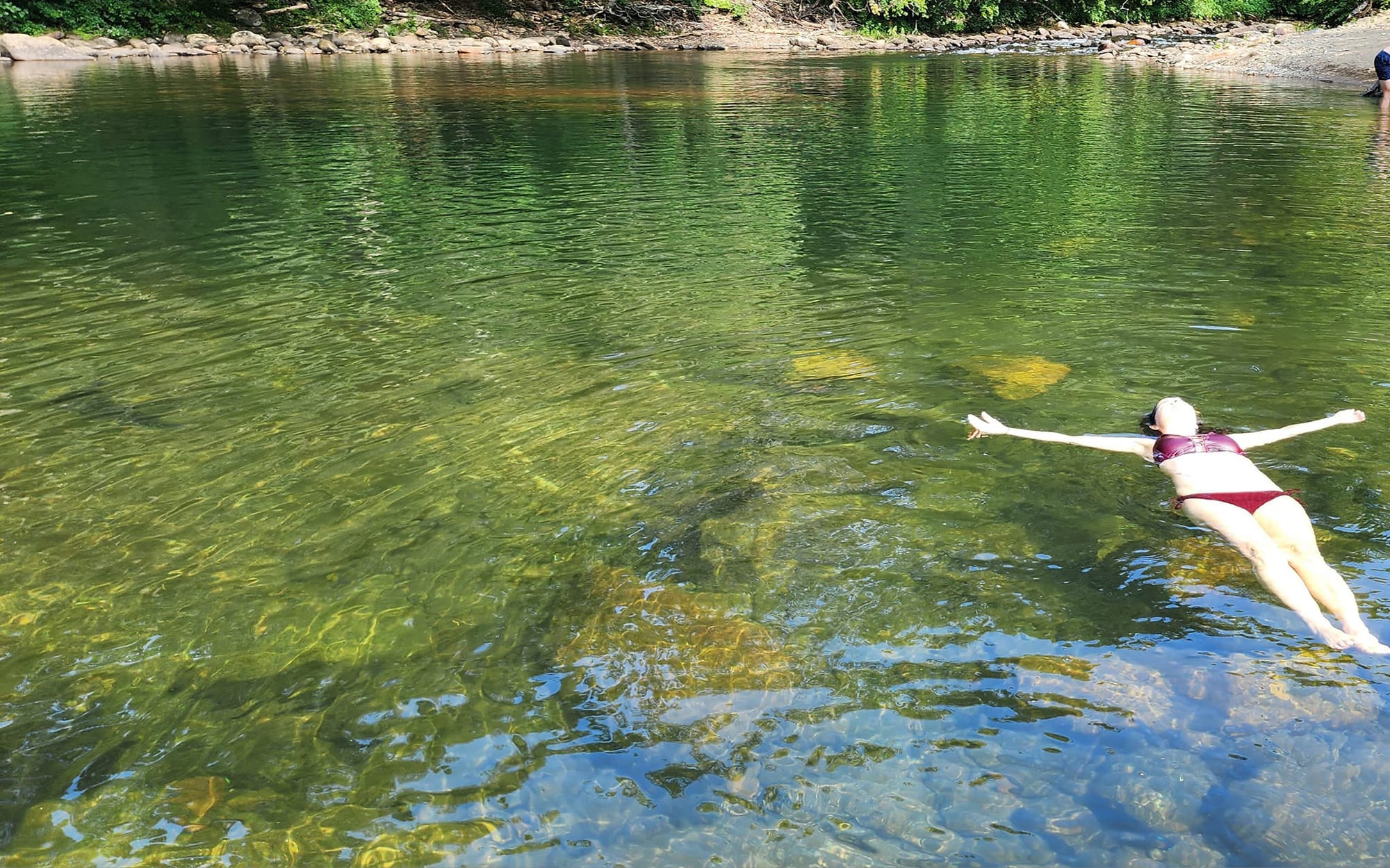 Briana floating weightlessly in a river swimming hole