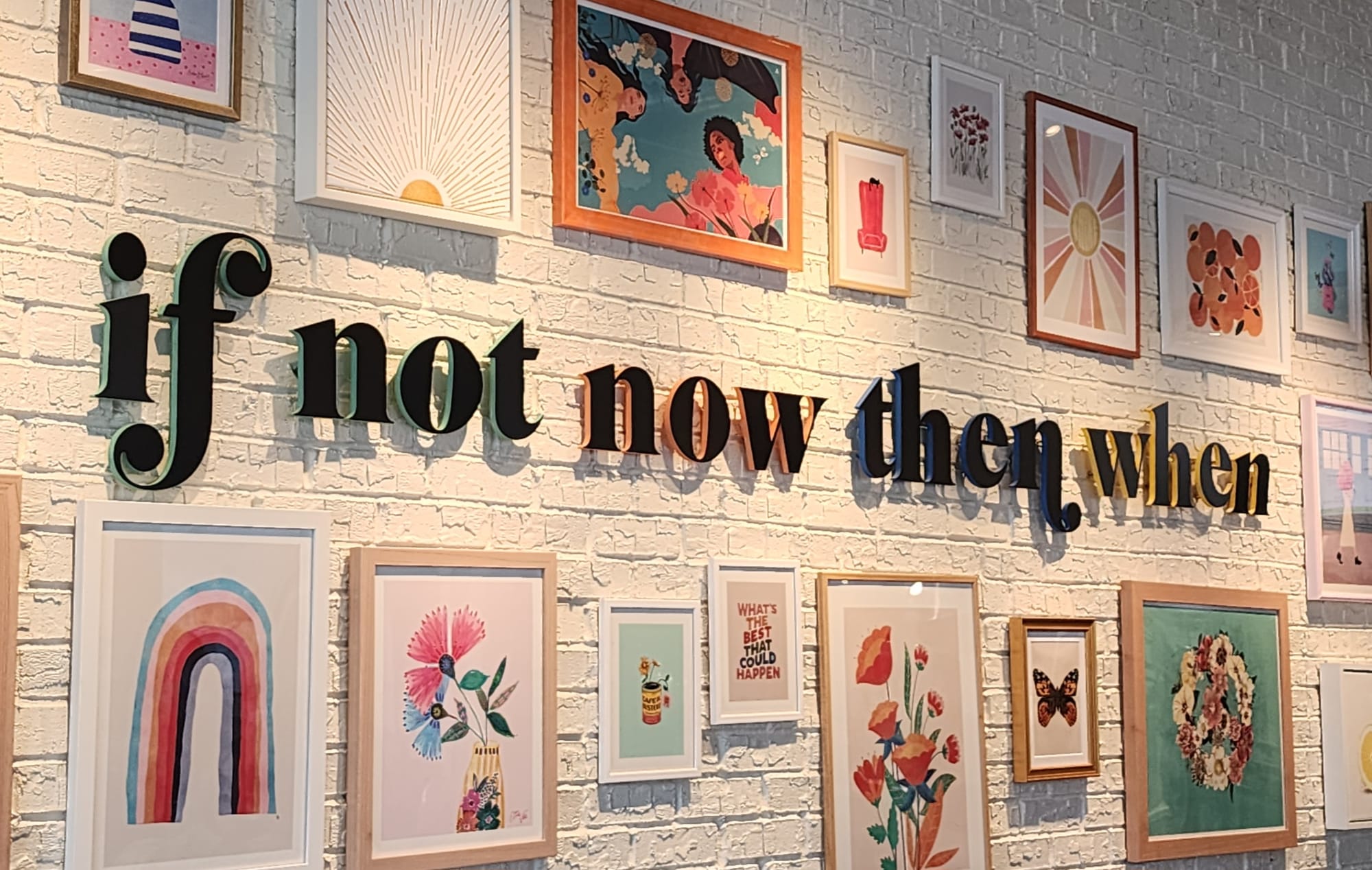 A wall reading If Not Now Then When, surrounded by framed art